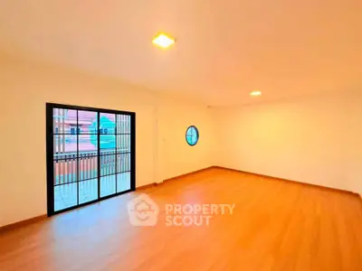 Spacious empty room with wooden flooring and large window offering natural light.