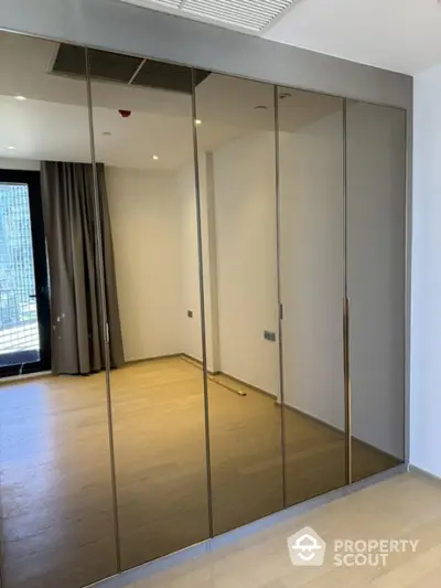 Spacious bedroom with mirrored wardrobe and wooden flooring in modern apartment.