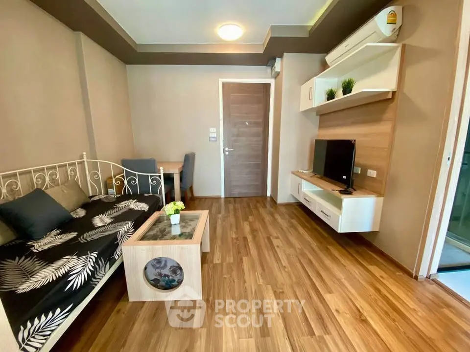Modern living room with stylish decor and wooden flooring, featuring a cozy seating area and wall-mounted TV.