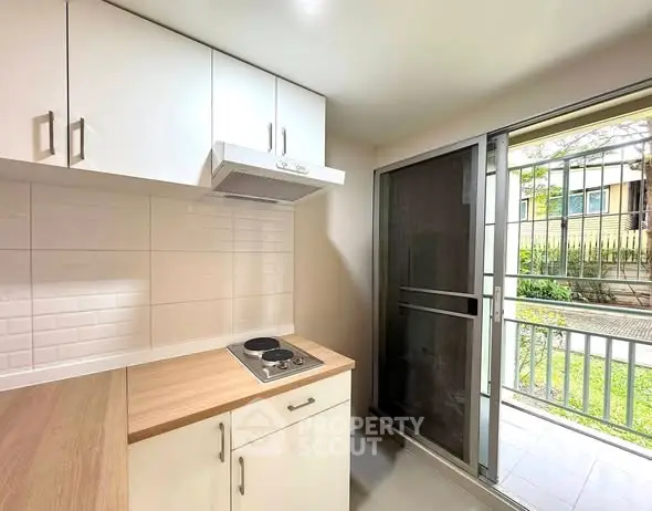 Modern kitchen with sleek cabinetry and electric cooktop, opening to a lush garden view.
