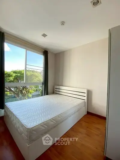 Bright bedroom with large window and wooden flooring, featuring a comfortable bed and serene outdoor view.