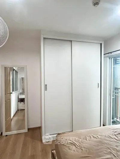 Modern bedroom with sliding wardrobe and mirror, featuring a cozy bed and natural light.