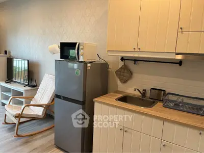 Modern kitchen with fridge, microwave, and stylish cabinetry in cozy apartment.