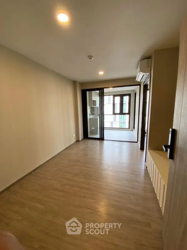 Spacious empty room with wooden flooring and large windows in modern apartment.
