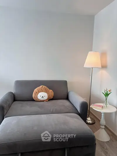 Cozy living room with plush gray sofa, stylish lamp, and elegant side table with flowers.