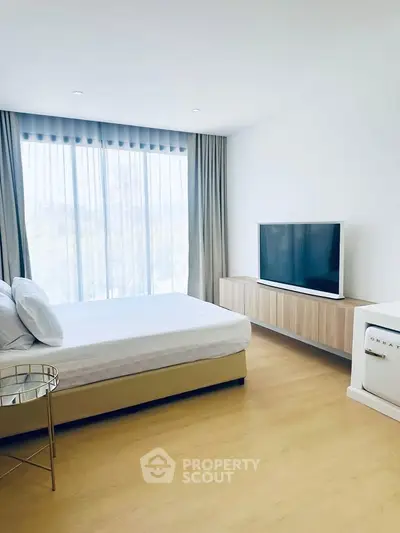 Modern bedroom with large window, stylish TV unit, and elegant decor in a bright, airy space.