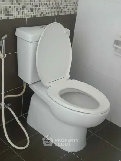 Modern bathroom with sleek toilet and bidet spray, featuring stylish tile design.