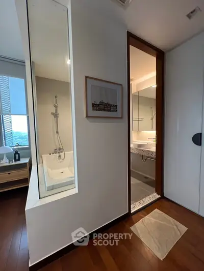 Modern bathroom with wooden flooring and glass partition, featuring a bathtub and sleek vanity.