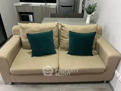 Cozy living room with beige sofa and teal cushions, adjacent to modern kitchen area.