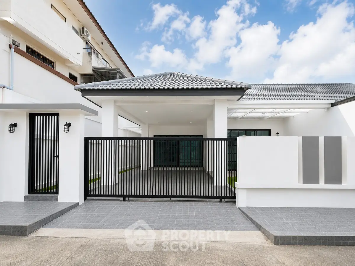 Modern single-story house with sleek black gate and tiled driveway under a clear blue sky.