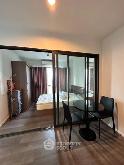 Modern bedroom with glass partition and dining area, stylish furniture and natural light.