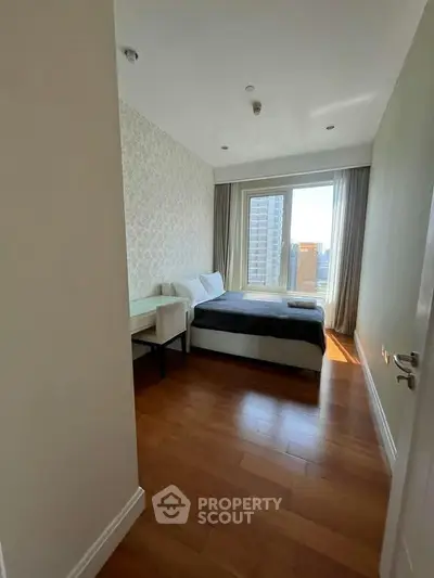 Modern bedroom with wooden flooring and large window offering city view