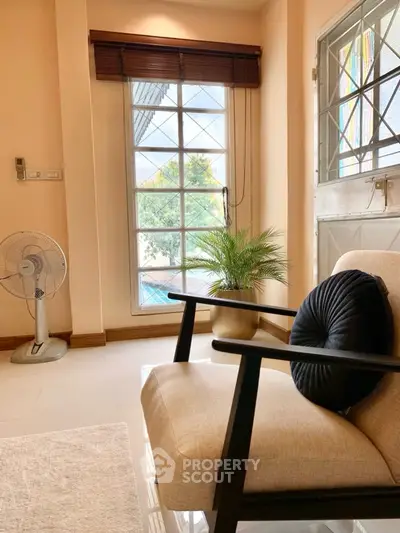 Cozy living room with armchair, fan, and large window offering garden view.