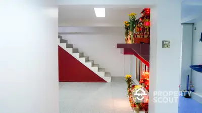 Bright and spacious home interior featuring a clean white aesthetic with a striking red staircase, complemented by vibrant floral decorations.