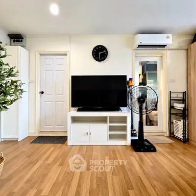 Modern living room with wooden flooring, TV setup, and air conditioning unit.