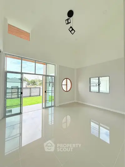 Spacious modern living room with high ceilings and large windows opening to a lush garden view.