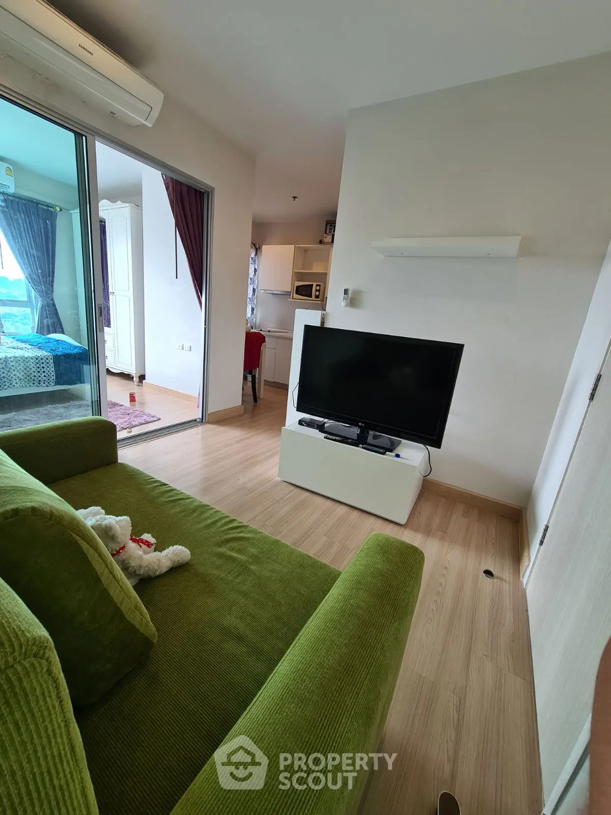 Modern living room with green sofa and TV, open layout to bedroom and kitchen