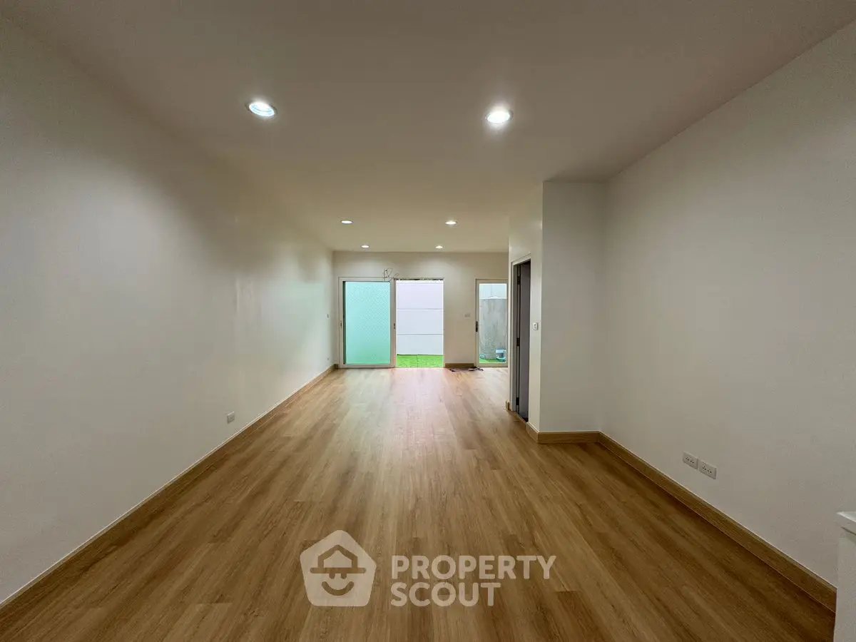 Spacious empty living room with wooden flooring and sliding glass doors to garden.