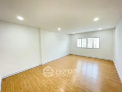 Spacious empty room with wooden flooring and large window, perfect for customization.