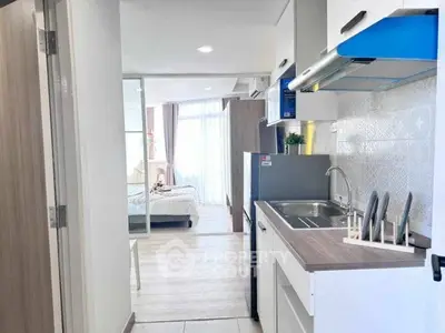 Modern compact kitchen with open layout leading to a bright bedroom with large windows.