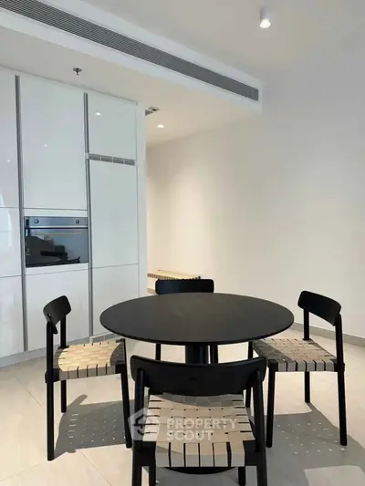 Modern dining area with sleek black table and chairs, integrated kitchen appliances, and minimalist design.