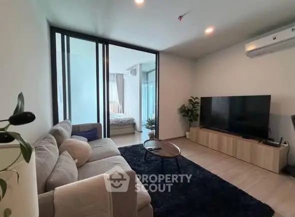 Modern living room with cozy sofa and large TV, open to a bright bedroom.