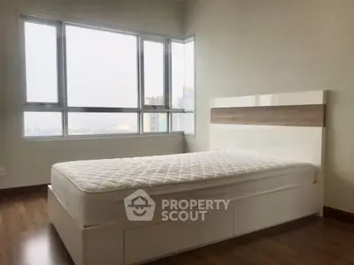 Modern bedroom with large windows and city view, featuring a sleek bed frame and wooden flooring.