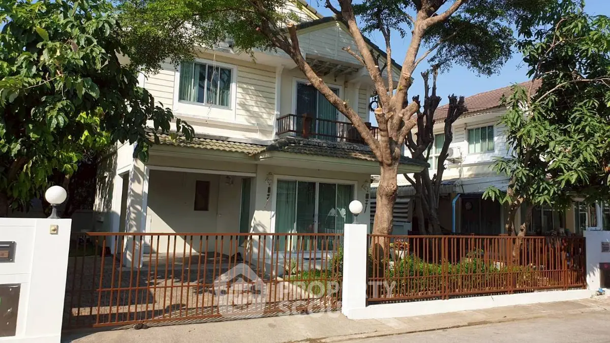 Charming two-story house with lush greenery and gated entrance in a serene neighborhood.