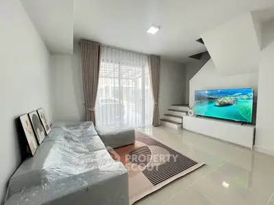 Modern living room with large TV, stylish sofa, and elegant staircase