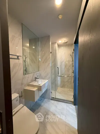 Modern bathroom with sleek fixtures and marble tiles, featuring a glass-enclosed shower and elegant sink.