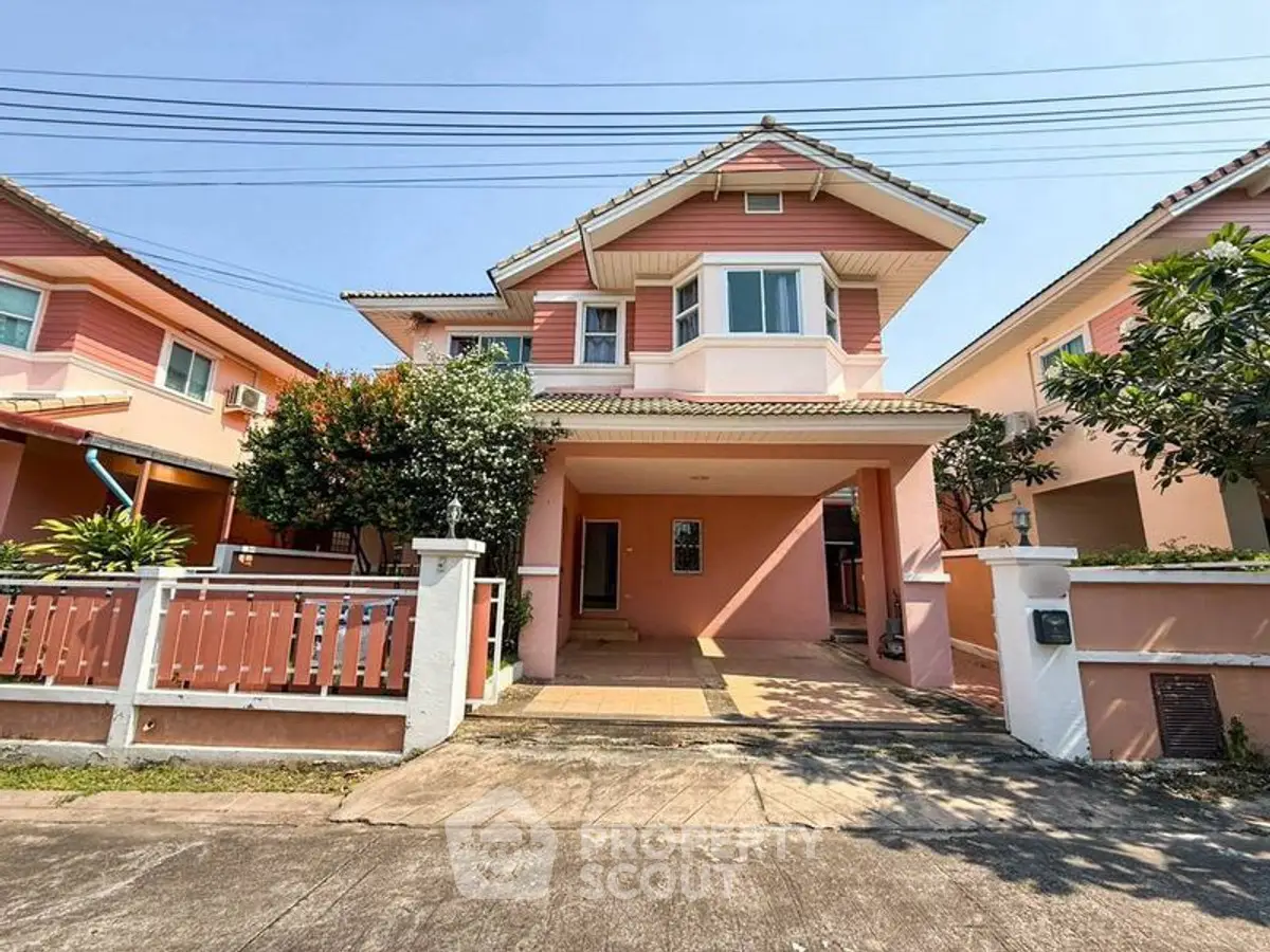 Charming two-story pink house with a spacious driveway and lush greenery in a serene neighborhood.