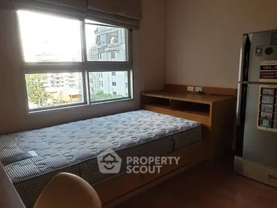Cozy bedroom with city view, featuring a single bed and modern refrigerator, perfect for urban living.