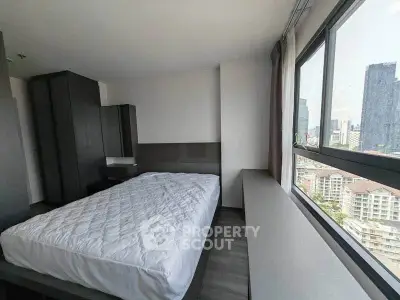 Modern bedroom with large windows offering city views, featuring sleek furniture and neutral tones.