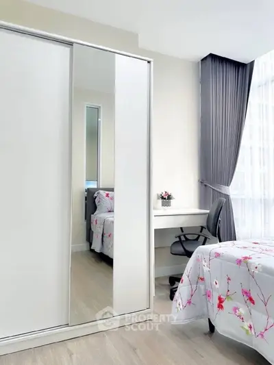 Bright bedroom with modern wardrobe, desk, and floral bedding in a high-rise apartment.