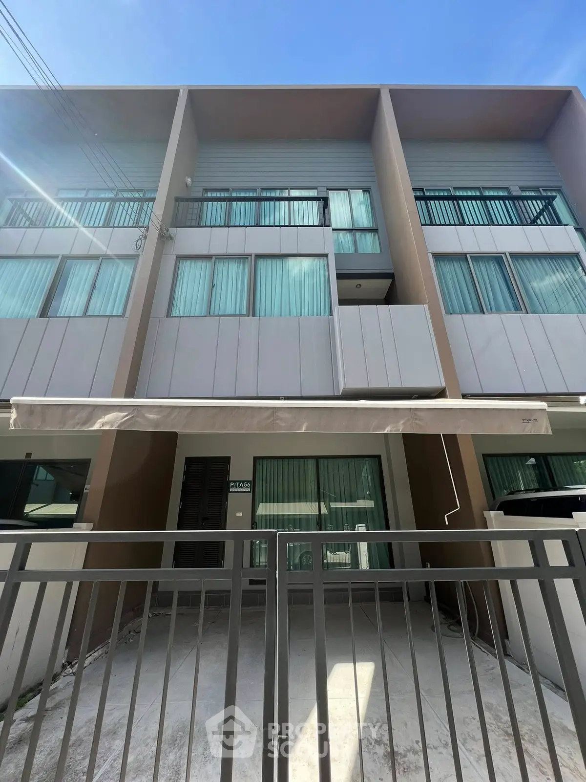 Modern townhouse with sleek facade and gated entrance under clear blue sky.