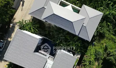 Aerial view of modern residential property with lush greenery and sleek roof design.