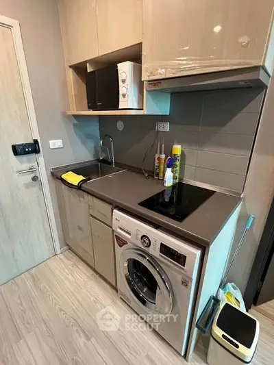 Compact modern kitchen with washing machine and microwave in stylish apartment.
