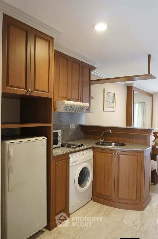 Charming kitchen with wooden cabinets, washing machine, and compact fridge in cozy apartment.