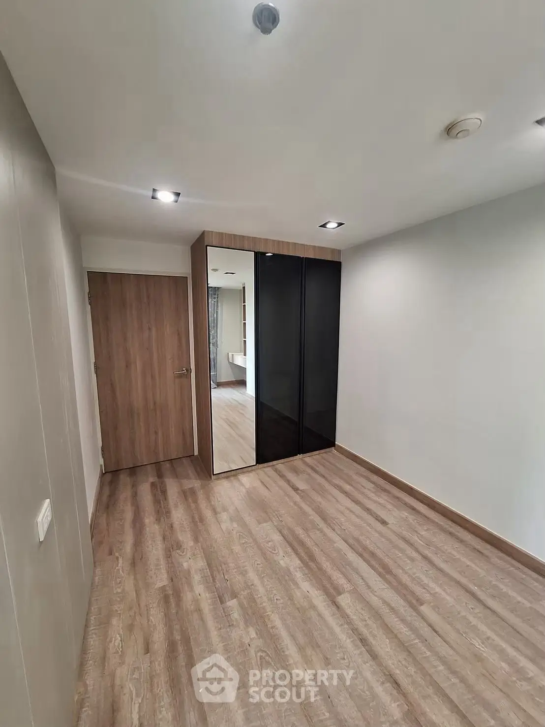Spacious empty bedroom with wooden flooring and mirrored wardrobe