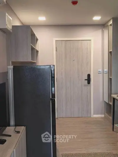 Modern apartment entrance with sleek wooden door and compact kitchen area.