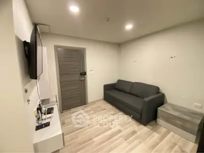 Modern living room with sleek gray sofa and wall-mounted TV, featuring stylish wood flooring.