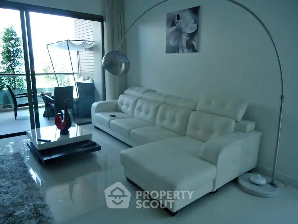 Luxurious modern living room with white leather sofa and elegant decor, opening to a spacious balcony with greenery.