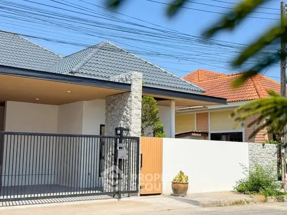 Modern single-story house with stone facade and gated entrance in a suburban neighborhood.