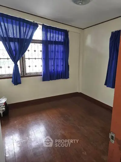 Cozy bedroom with wooden floors and blue curtains in a well-lit space.