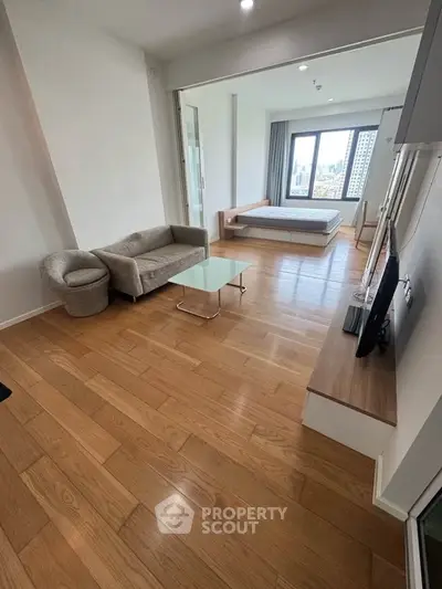 Modern open-plan living room with wooden flooring and city view, featuring cozy seating and sleek TV setup.