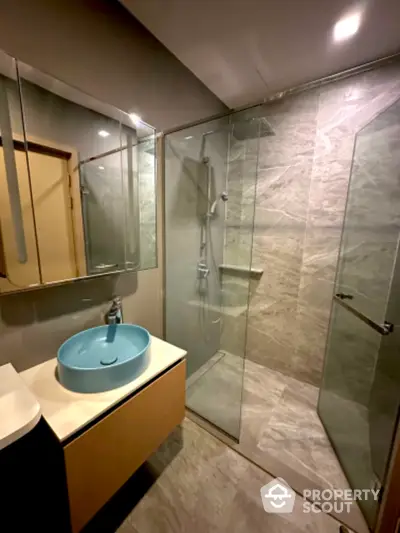 Modern bathroom with sleek glass shower enclosure and unique blue basin atop a stylish vanity, complemented by neutral toned tiles.