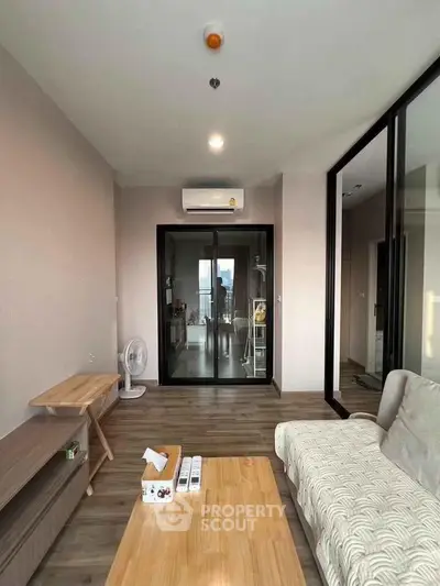 Modern living room with sleek design and large glass doors leading to a balcony, featuring cozy furniture and wooden flooring.