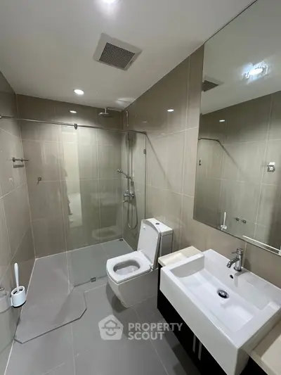 Modern bathroom with glass shower and sleek fixtures in contemporary apartment.