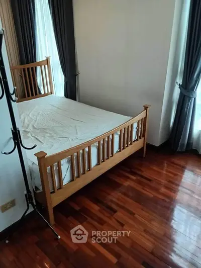 Cozy bedroom with wooden bed frame and polished hardwood floors, featuring elegant curtains for a serene ambiance.