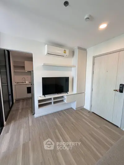 Modern living room with sleek design, featuring built-in TV unit and air conditioning, adjacent to a compact kitchen.